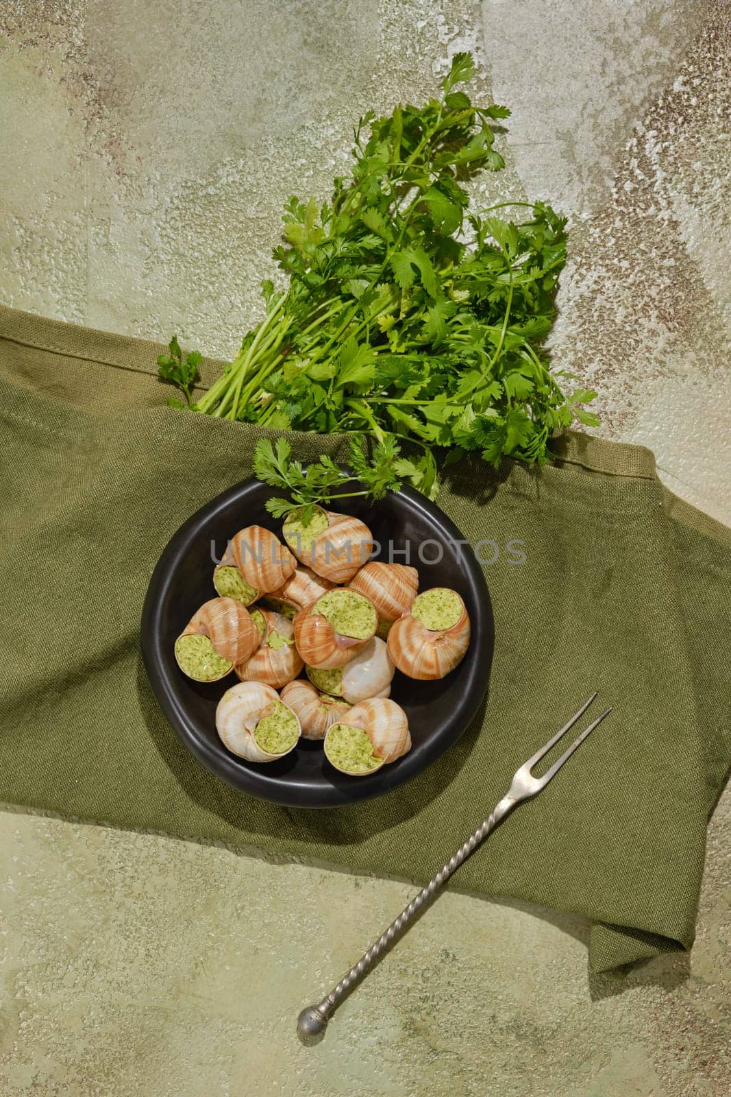 Overhead composition of edible snails baked in sauce and filled with herbal spicy butter on a plate