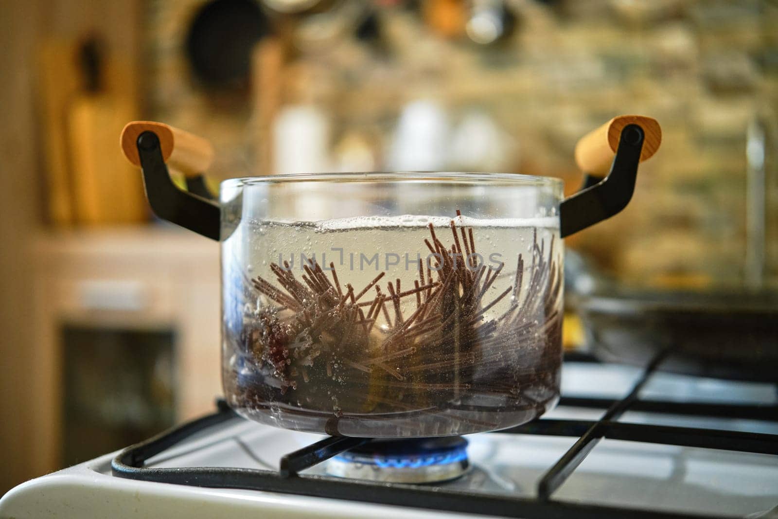 Close-up view of boiling black rice noodles in transparent glass saucepan on a gas stove