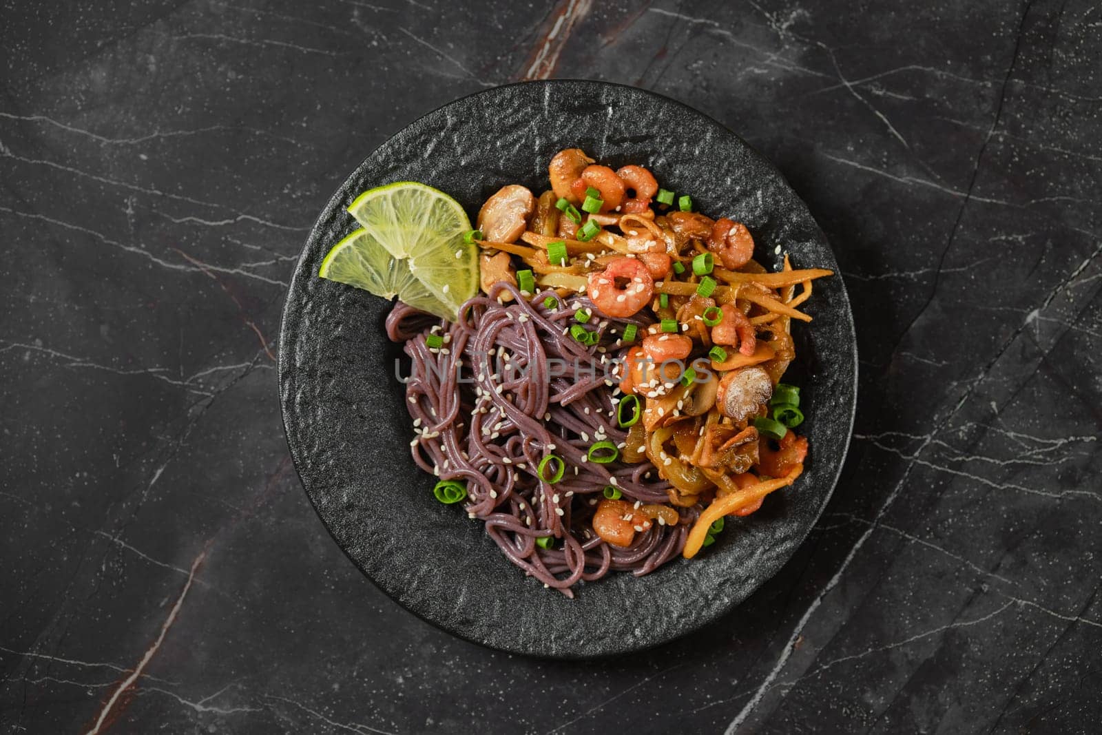 Overhead view of stone plate with spicy black rice noodles and shrimps