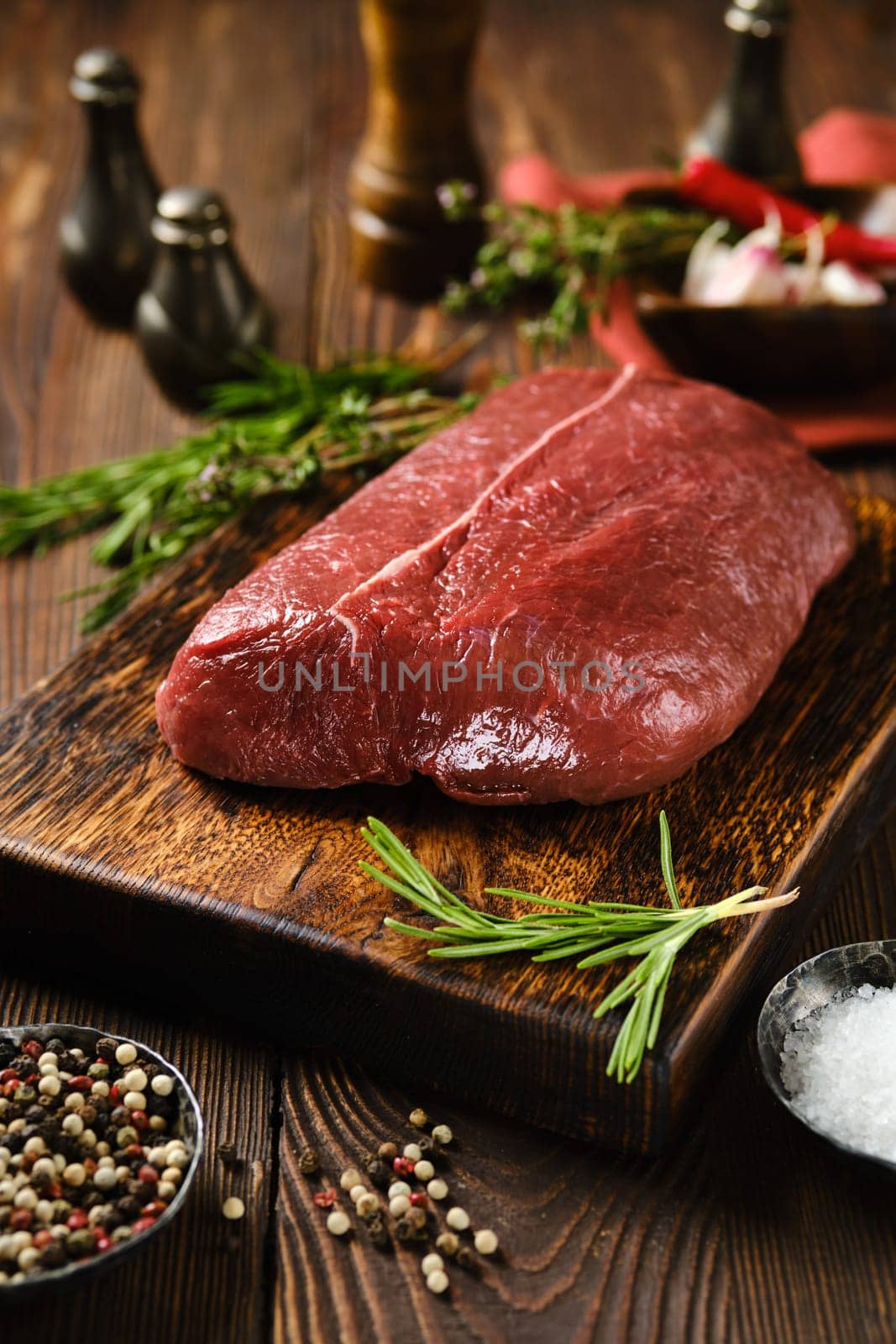 Raw beef top round steak on wooden cutting board surrounded with spice and herbs