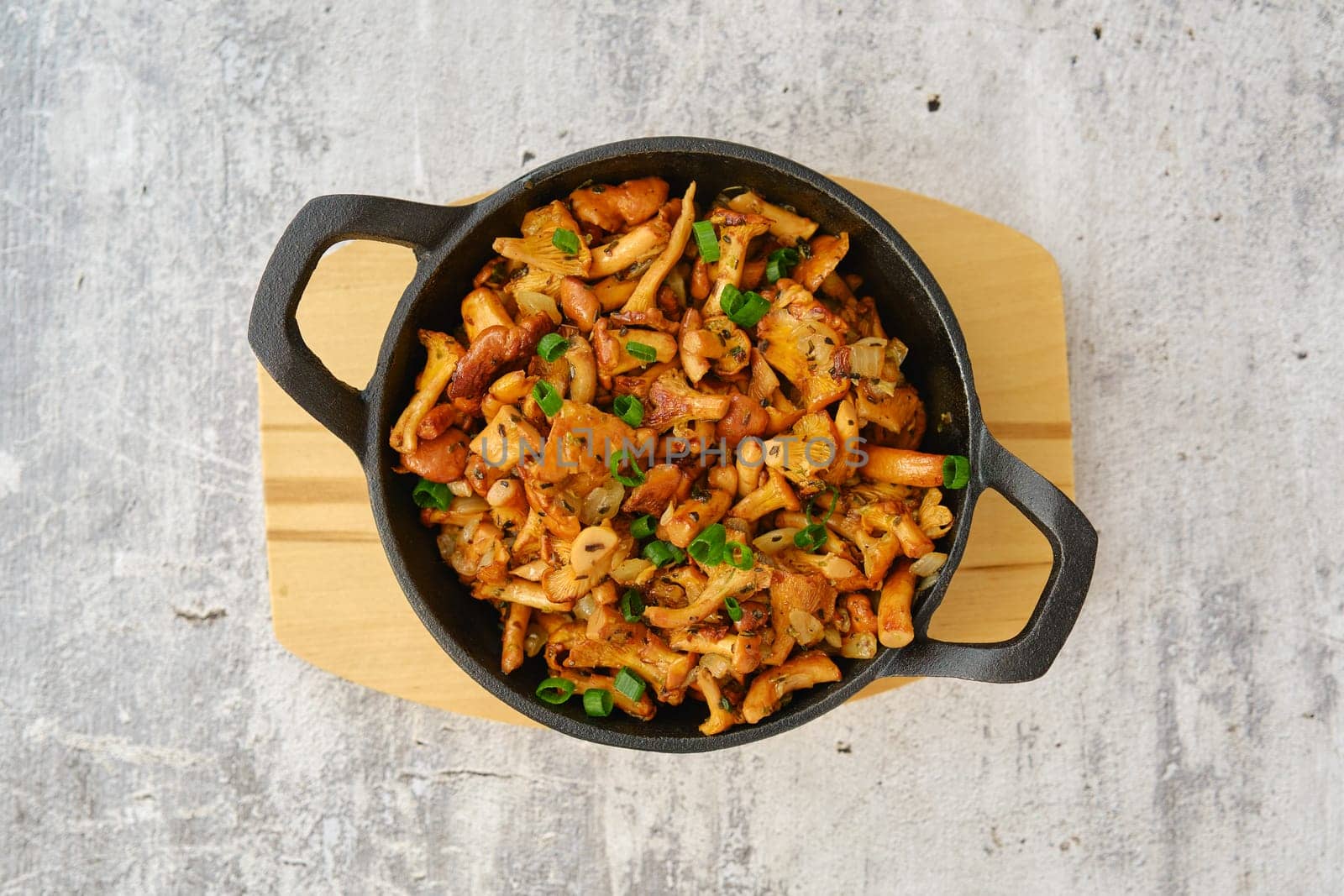 Overhead view of wild chanterelle mushrooms fried with thyme and spring onion in a cast iron skillet