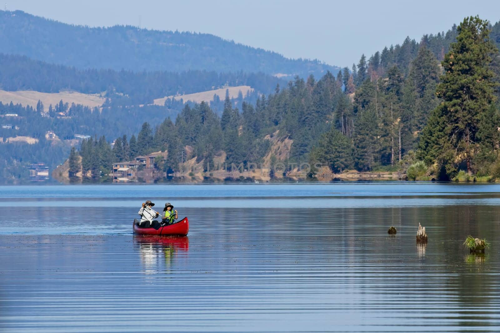 An editorial photo of a mature couple paddling the canoe on Coeur d'Alene Lake in north Idaho.