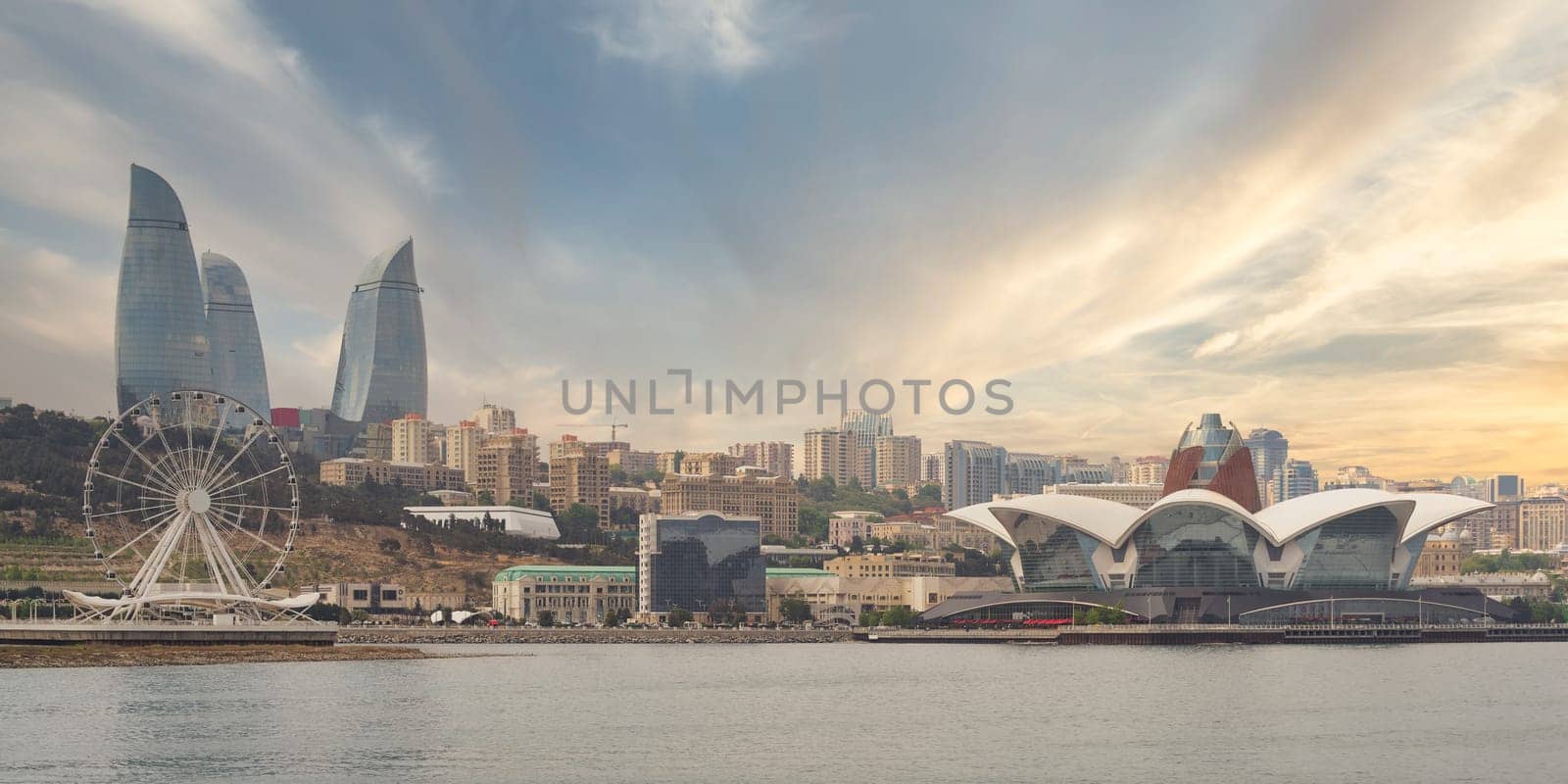The Baku Eye and Flame Towers rise majestically beside Deniz Mall, reflecting the vibrant atmosphere of Baku, Azerbaijan, at sunset