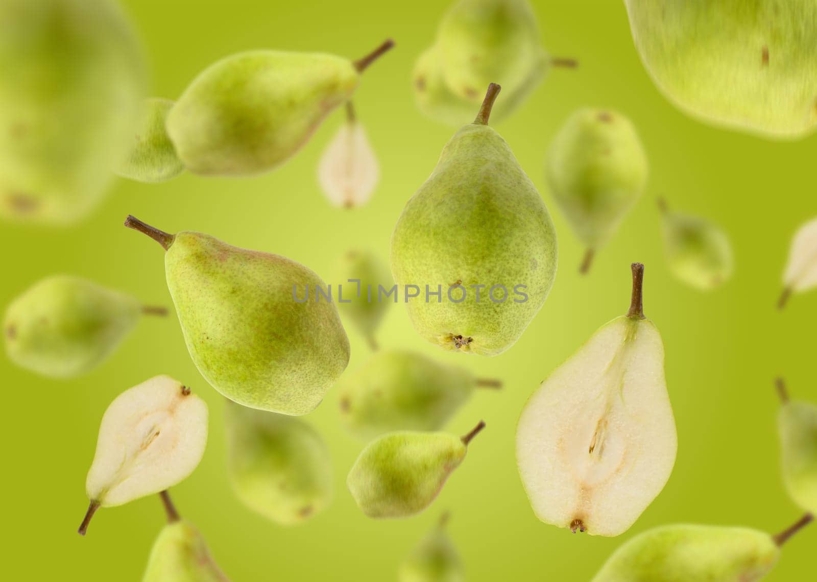 Halves and whole green pears levitate on a green background