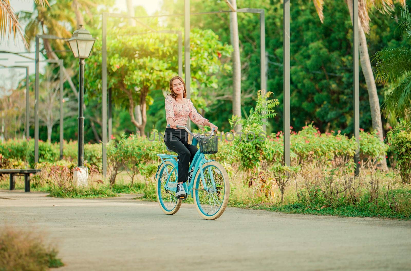 Happy girl riding a bicycle in a park at sunset. Portrait of smiling young woman riding a bicycle in a nice park