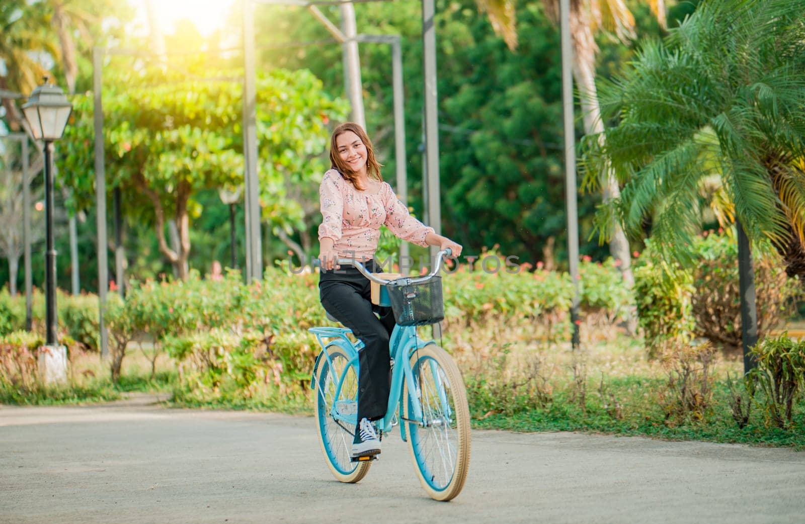 Portrait of smiling young woman riding a bicycle in a nice park. Happy girl riding a bicycle in a park at sunset