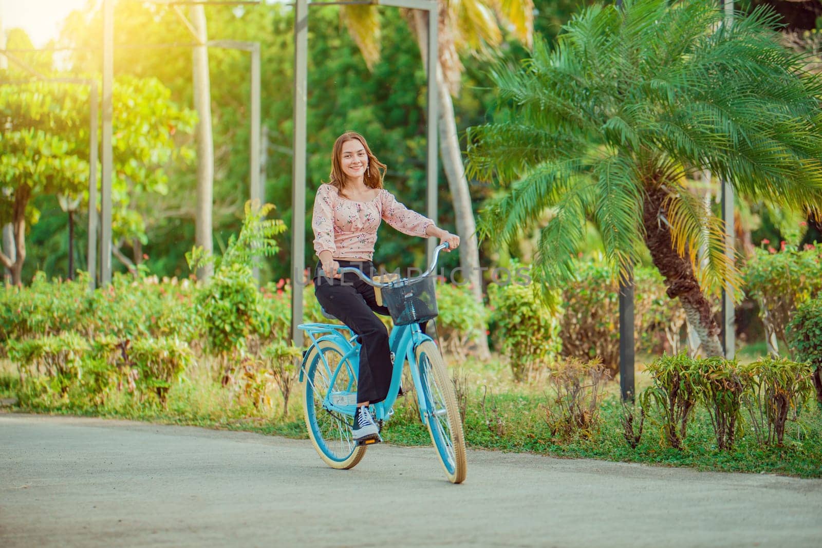 Cheerful Latin girl riding a bicycle in a green park. Beautiful and smiling young woman riding a bicycle in a nice park, looking at camera