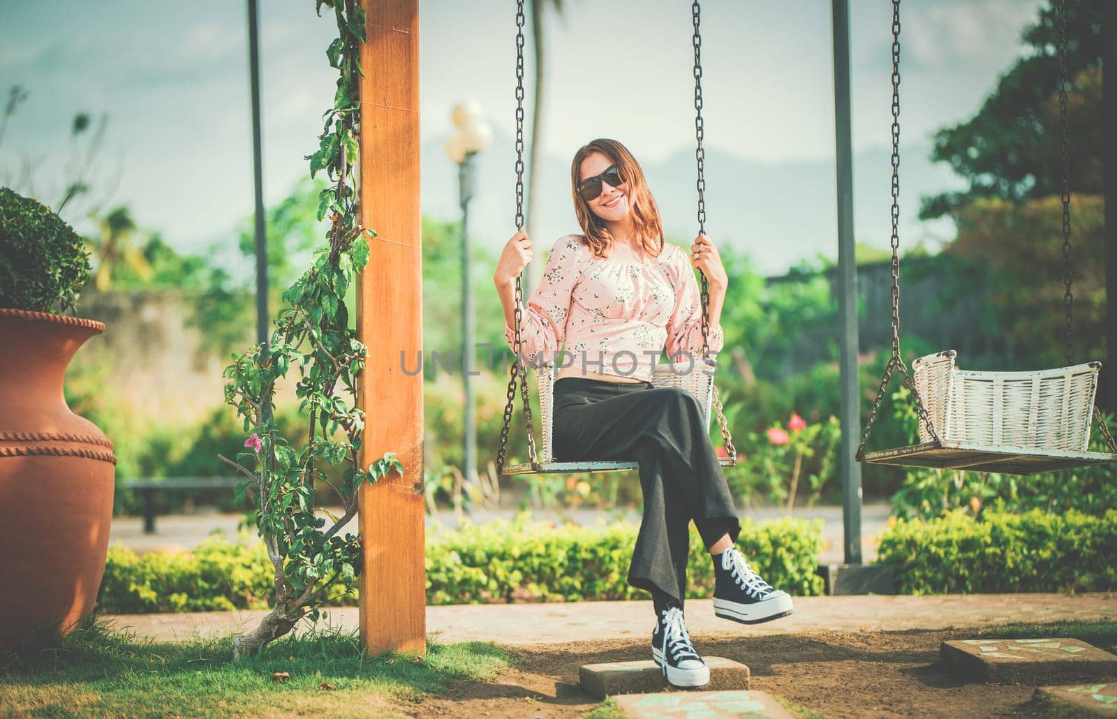 Happy young woman sitting on a swing in a nature park. Portrait of a smiling girl sitting on a swing in a nature park