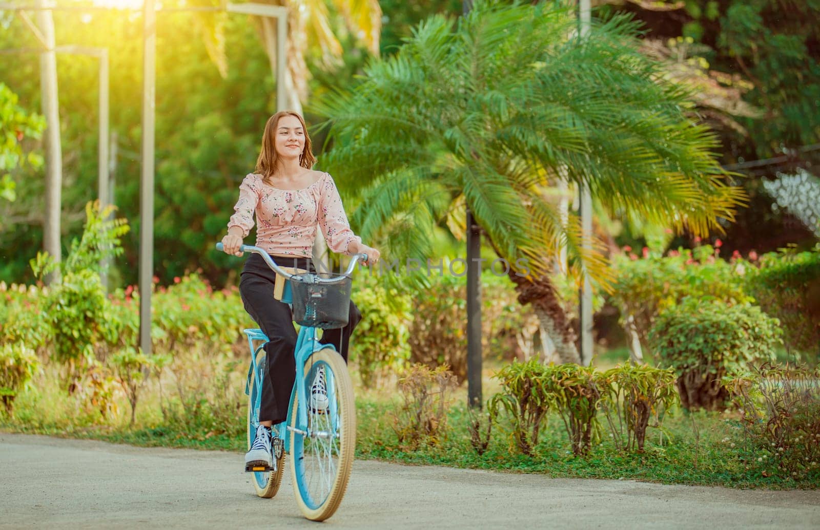 Beautiful and smiling young woman riding a bicycle in a nice park, looking at camera. Cheerful Latin girl riding a bicycle in a green park