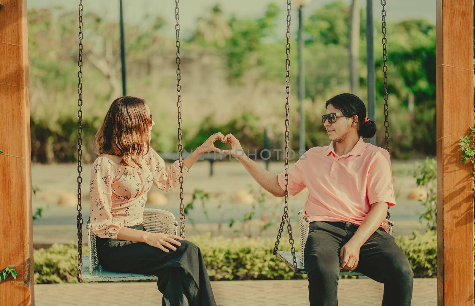 Young couple in love sitting on a swing making a heart shape. Happy couple in love on a park swing making a heart shape