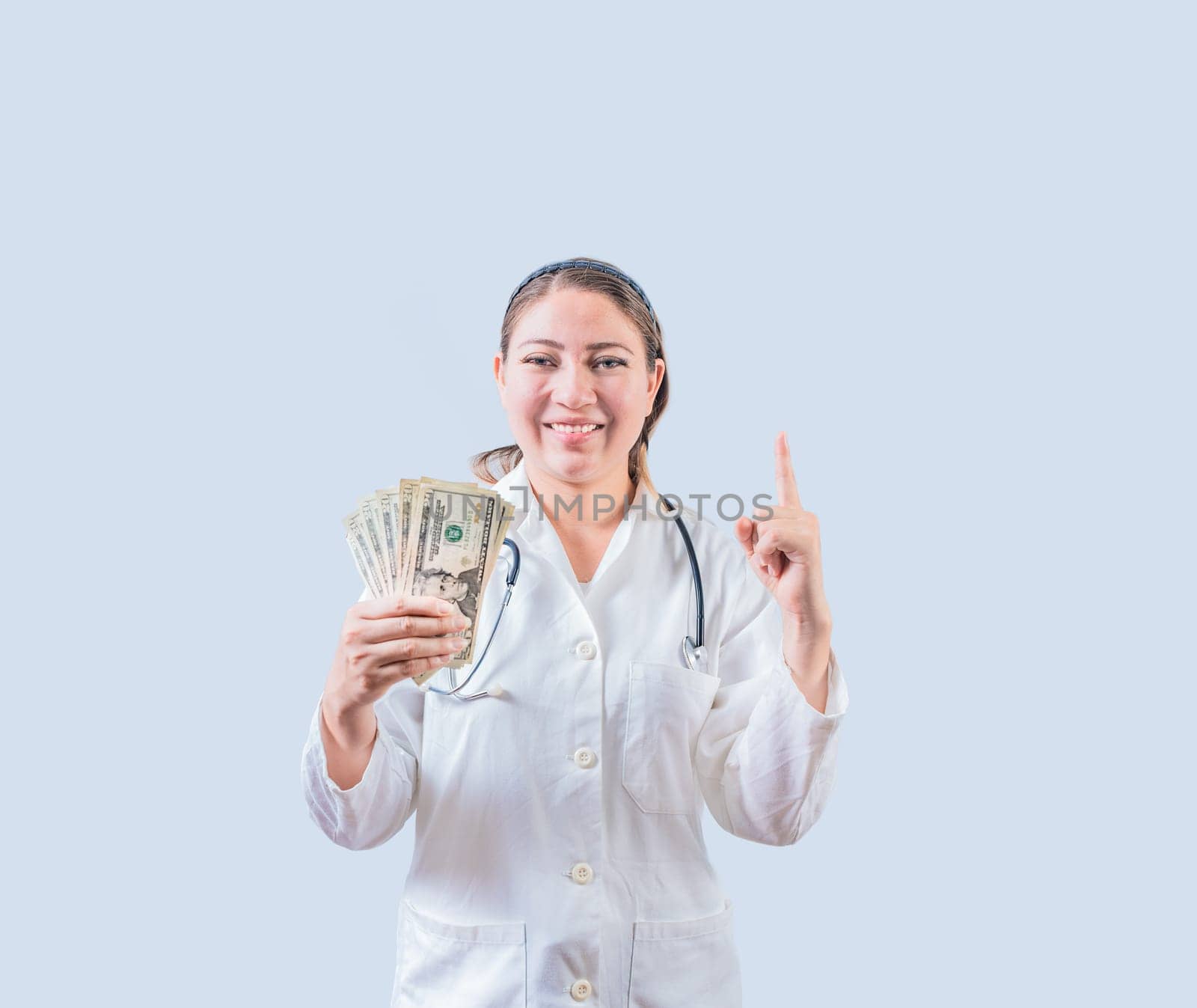 Smiling female doctor holding money and pointing up isolated. Happy young female doctor showing money and pointing at promo up