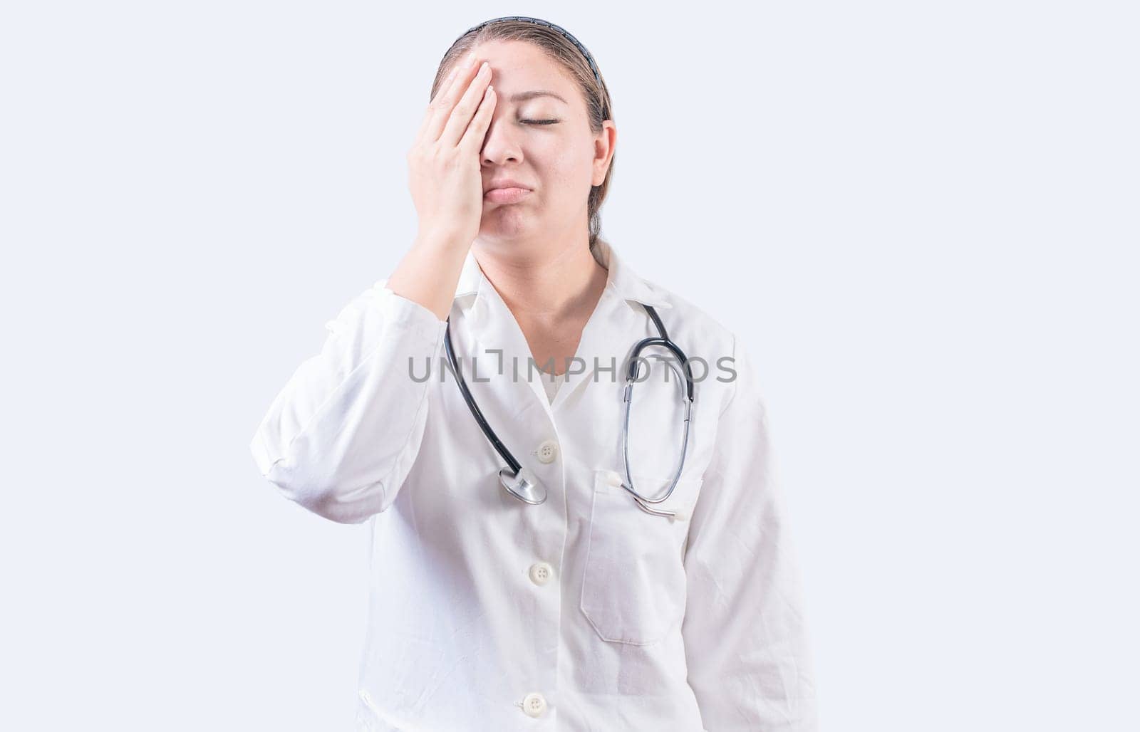 Stressed female doctor with hand on forehead isolated. Exhausted young female doctor with hand on forehead