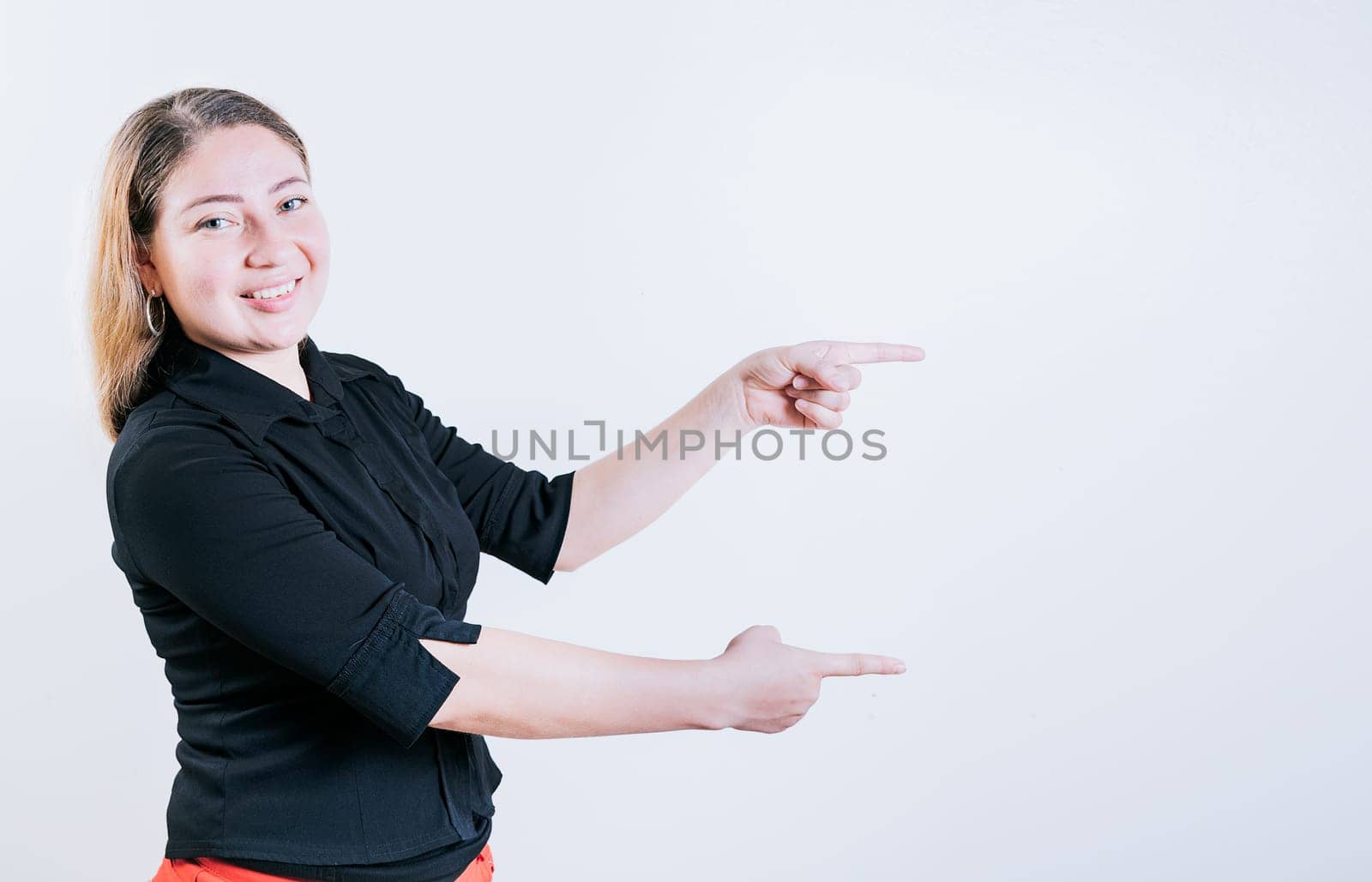 Happy latin woman pointing a promo isolated. Cheerful girl pointing an offer isolated. Beautiful young girl pointing to a banner to the side