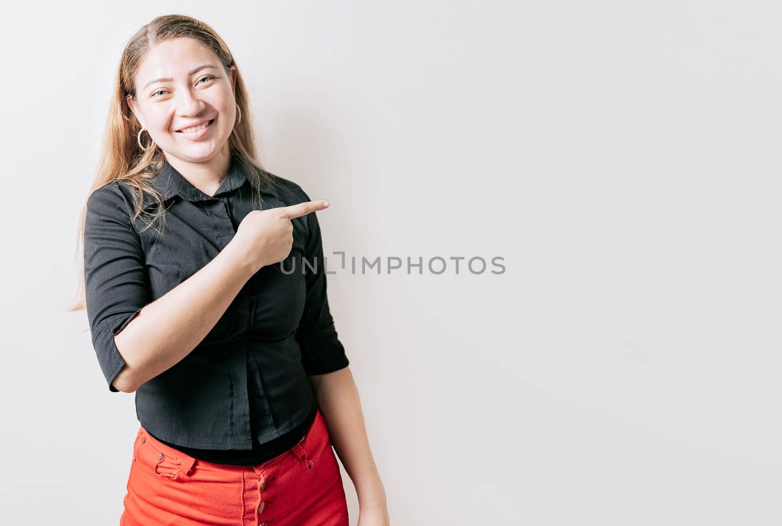 Smiling attractive young woman pointing an advertising isolated. Beautiful young girl pointing to a banner to the side. Happy latin woman pointing a promo