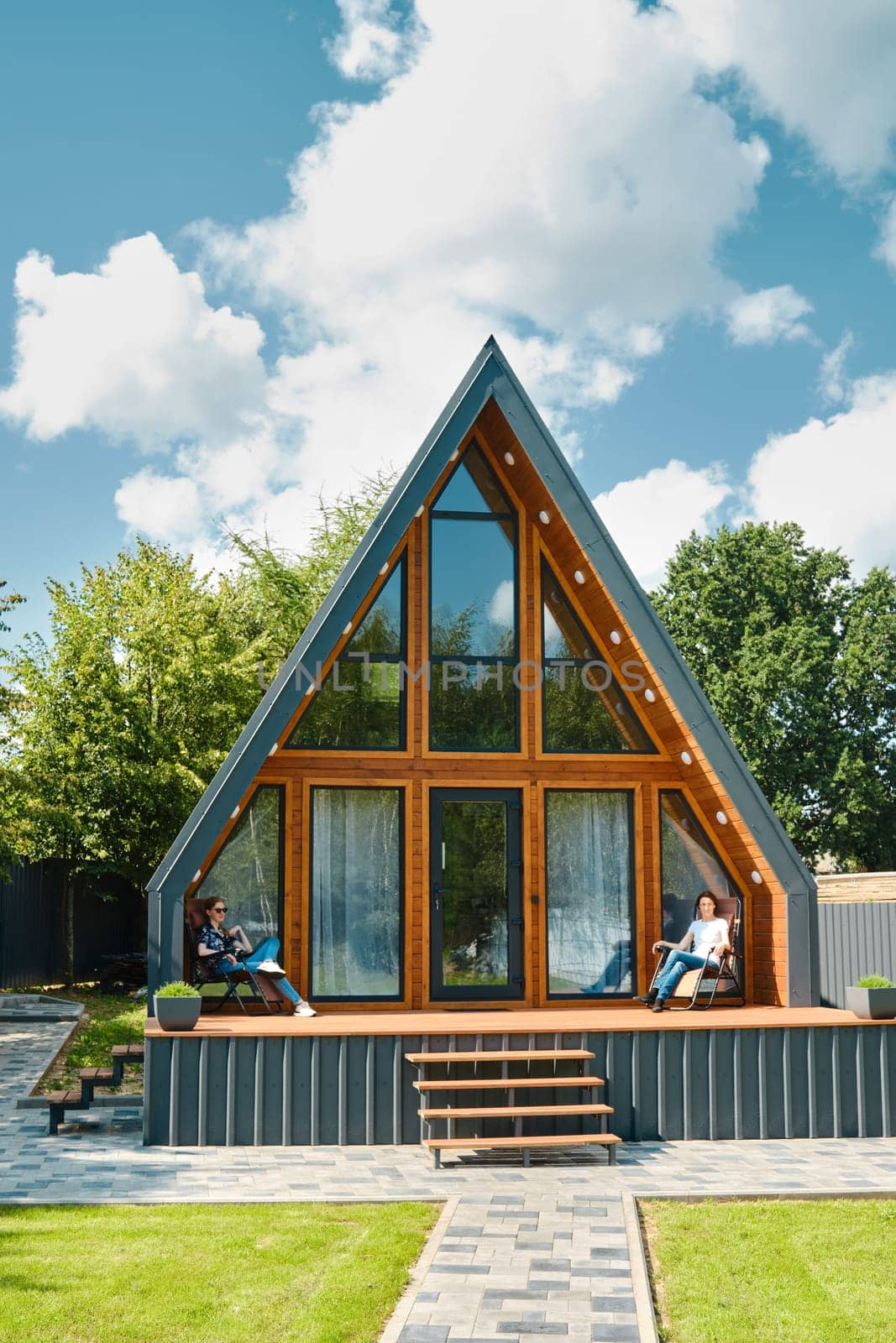 Mother and daughter sitting on a folding chairs on the terrace of a tiny triangular house