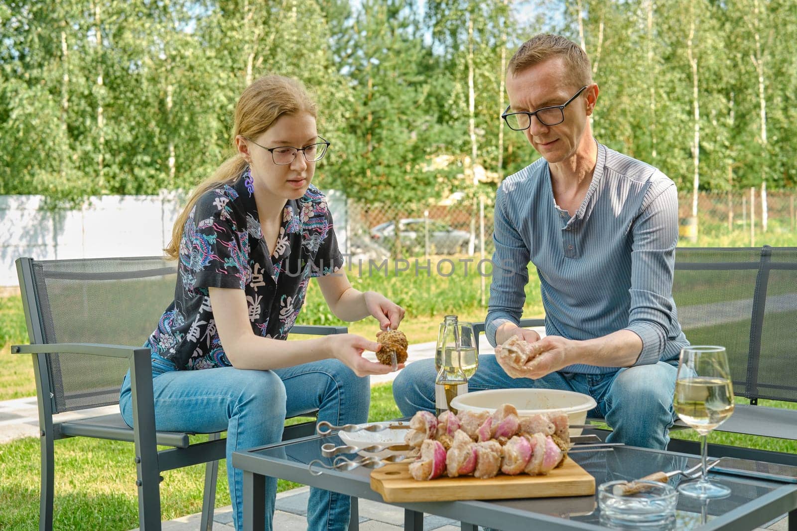 Father and daughter skewering meat and mushroom while sitting in the backyard