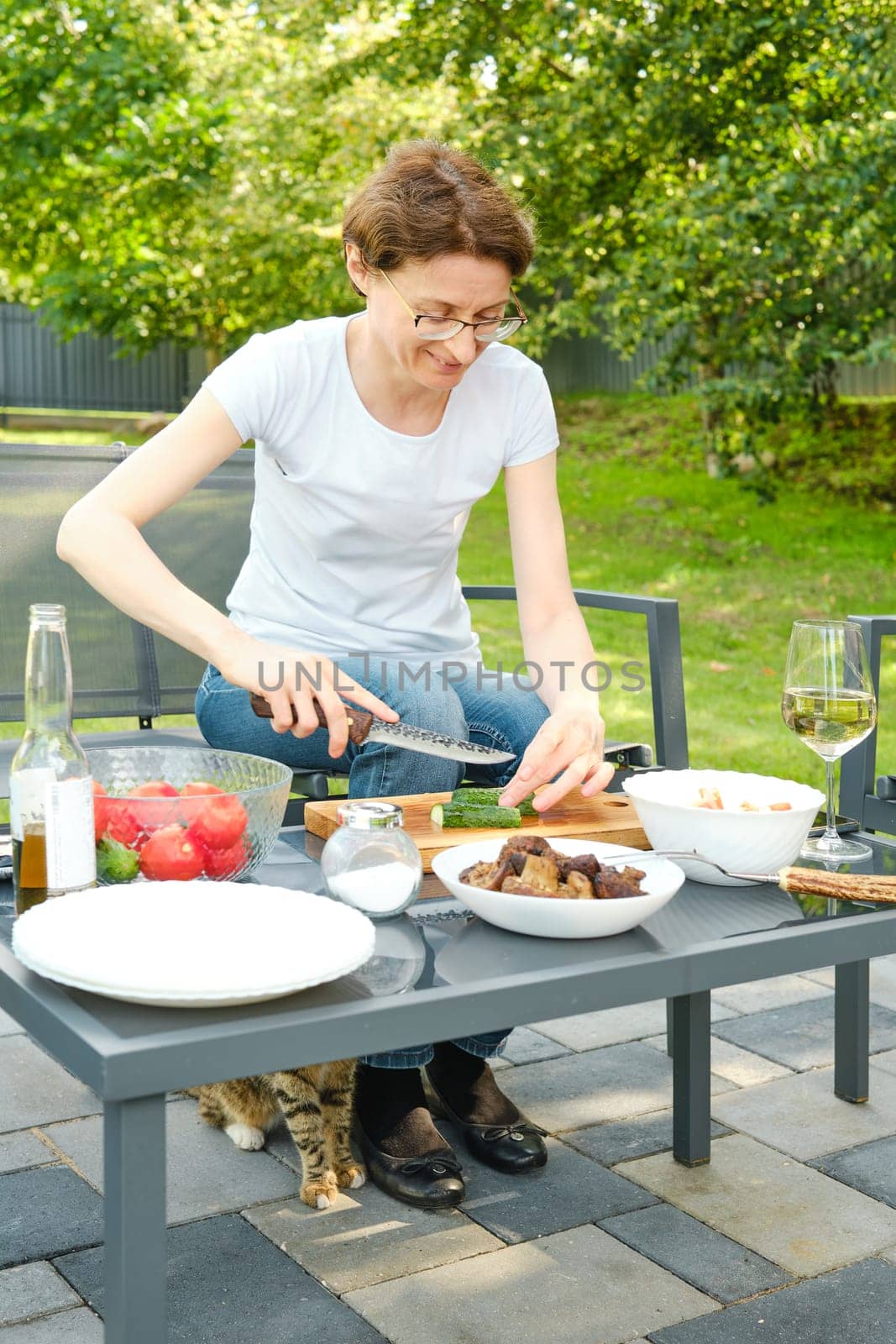 Middle-aged woman preparing salad outdoors while sitting in backyard