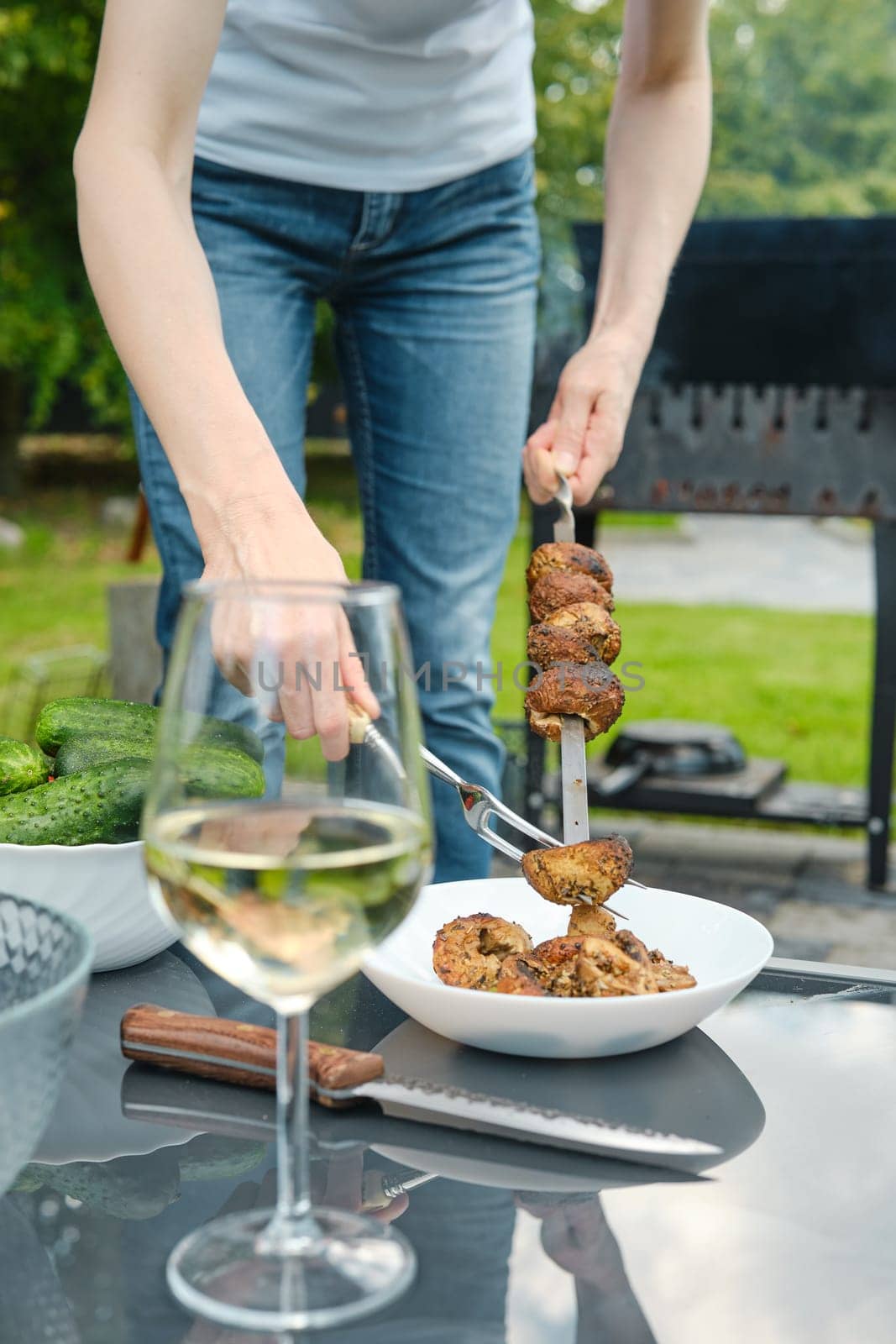 Unrecognizable woman removes grilled champignons from a skewer with a fork