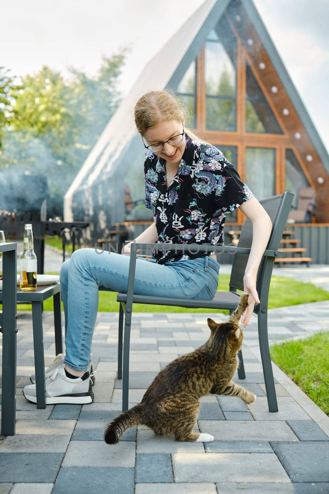 Girl plays with a cat while relaxing on the lawn of a country house during a picnic