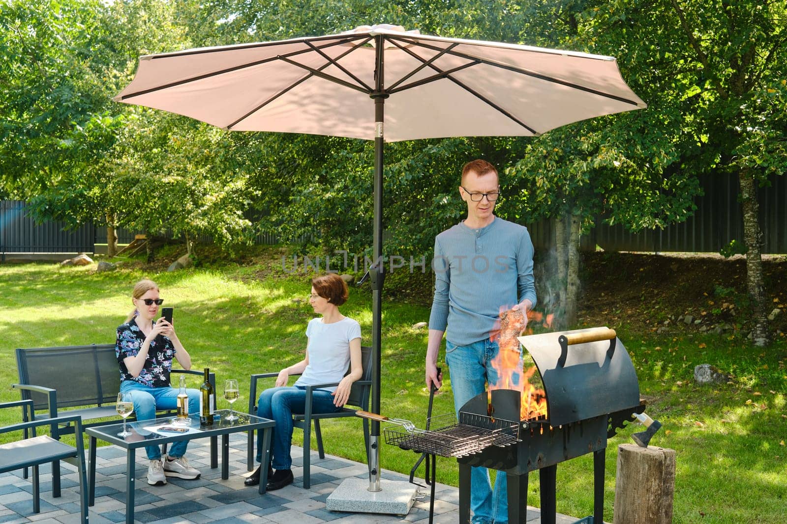 The daughter takes a photo of her father putting a birch log on the grill