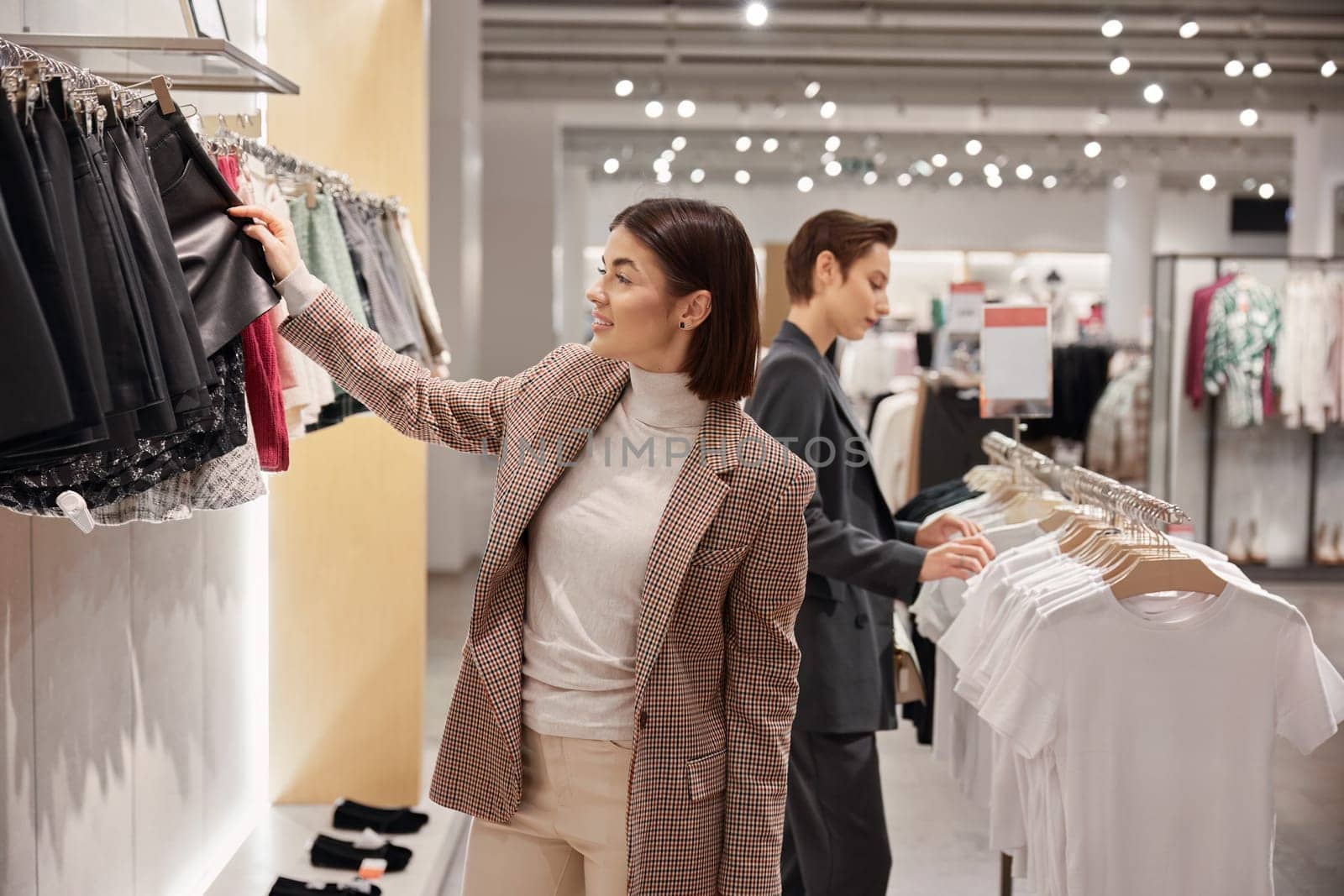 Two elegant woman enjoying shopping at fashion clothes boutique. Adult female friends searching trendy outfit together. Sale and consumerism concept