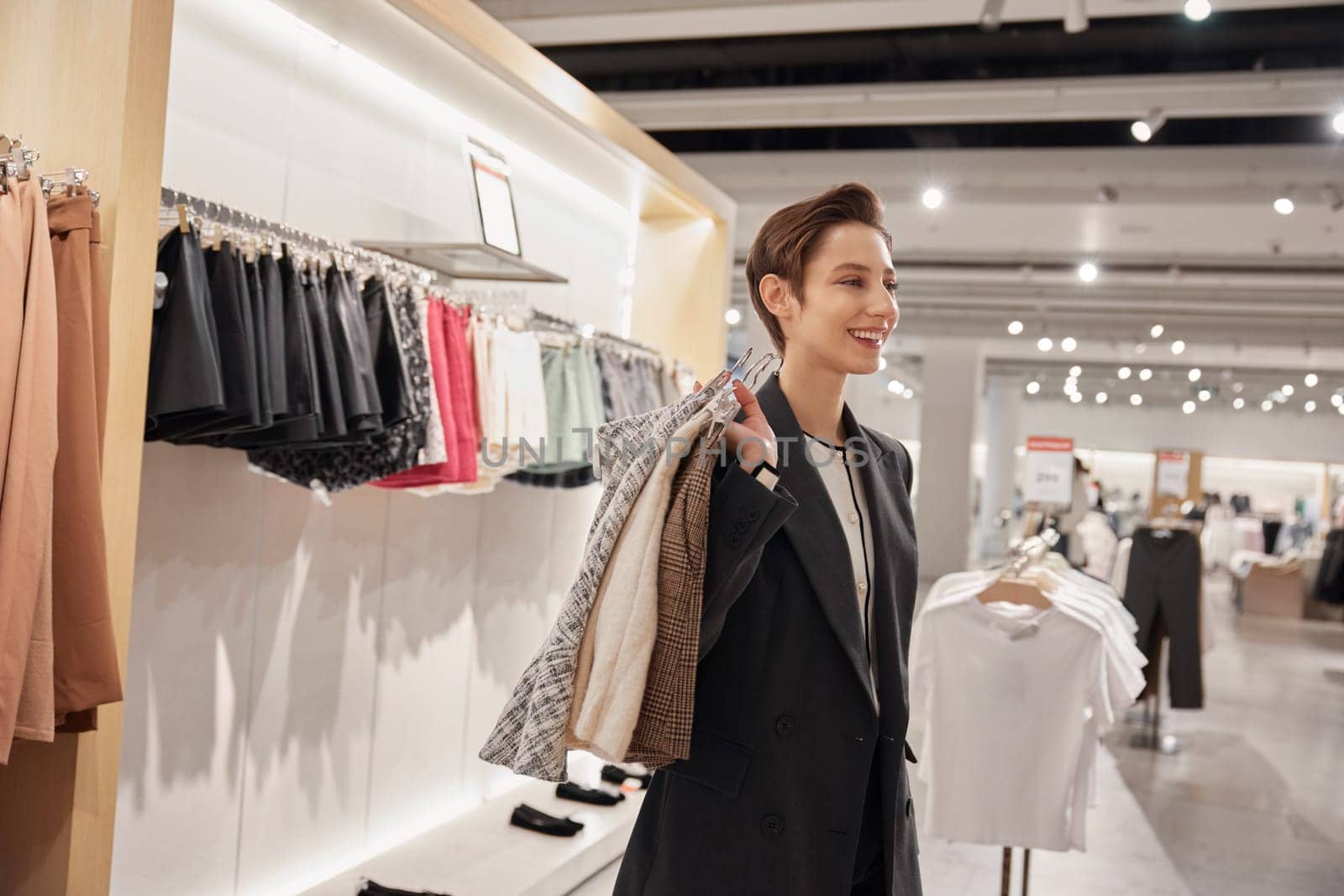 Portrait of young woman shopper holding stack of trendy fashion clothes. Big assortment and new collection arrival in fashion store