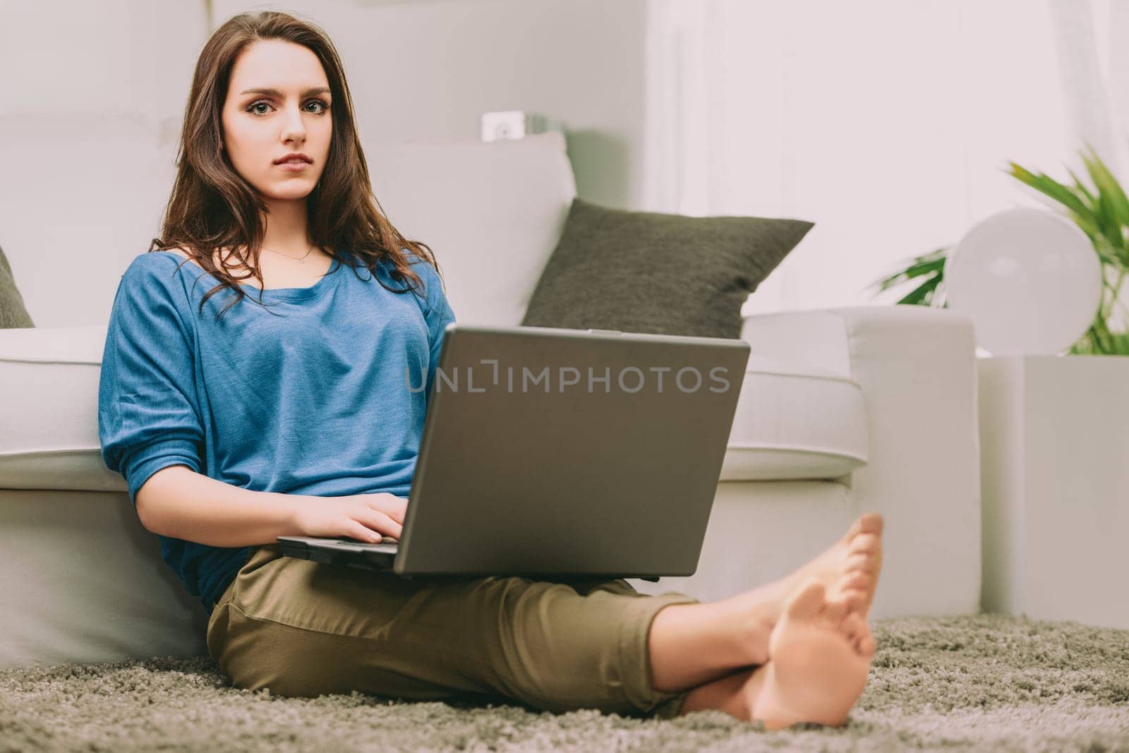 woman, dressed casually in a blue shirt, sits with her laptop, reflecting on future uncertainties. Her pensive gaze suggests a deep inner dialogue about work-life balance and societal expectations