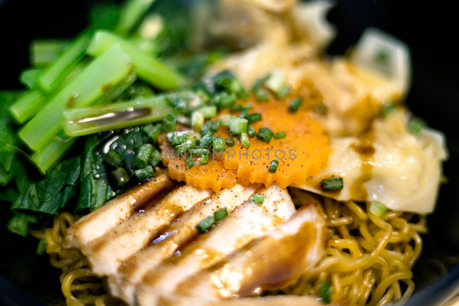 Egg noodle with roasted pork and shrimp wonton in black bowl.
