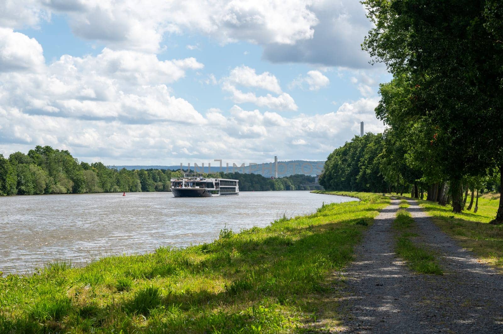 A pleasure boat sails along a river, with green nature, blue sky and white clouds