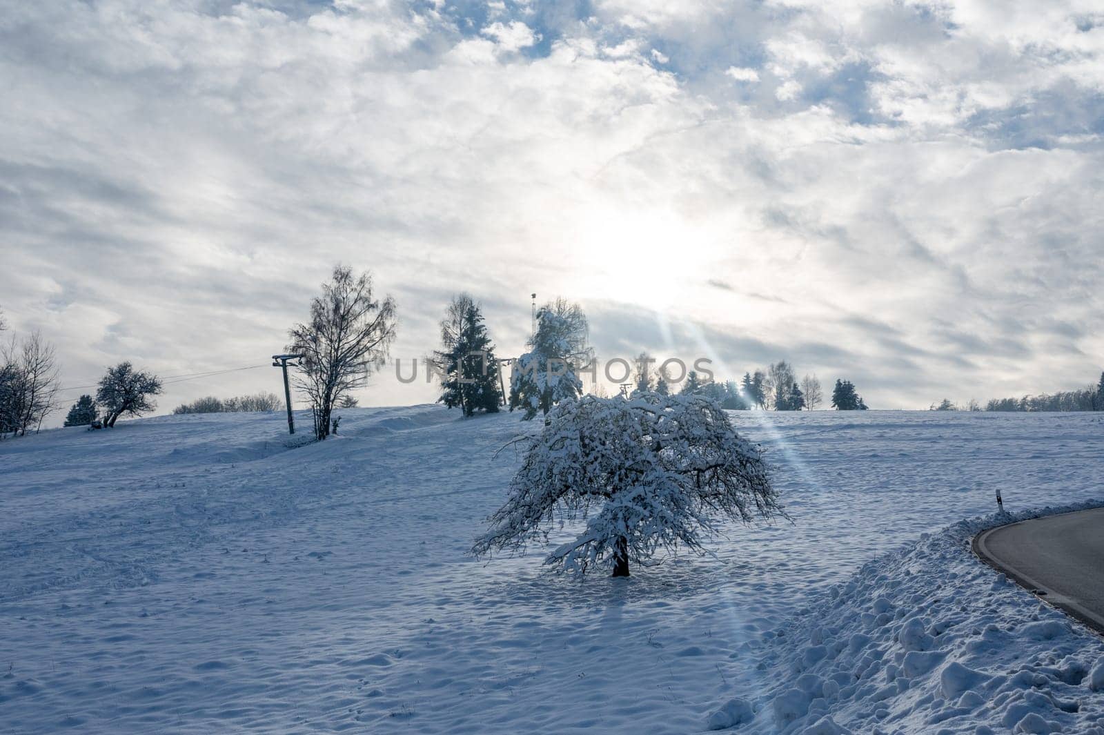 Ski resort at Engländer in Spessart, Bavaria, Germany. With a tree full of snow in the foreground and bright sun