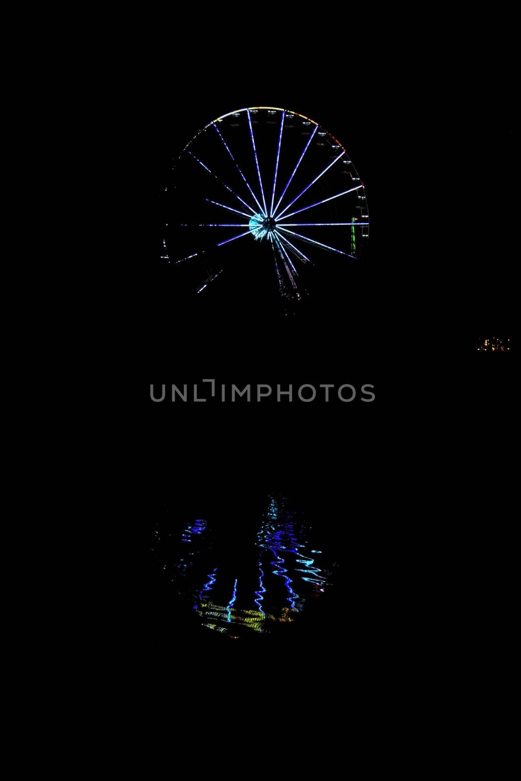 Ferris wheel with colorful lighting at dark night and reflections in the water