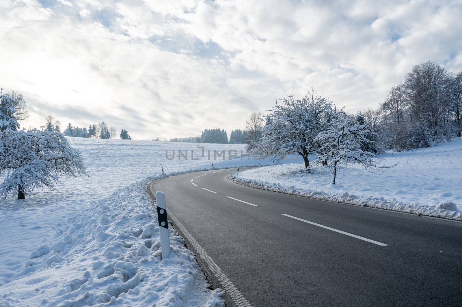Snow landscape with trees, road and blue sky with clouds