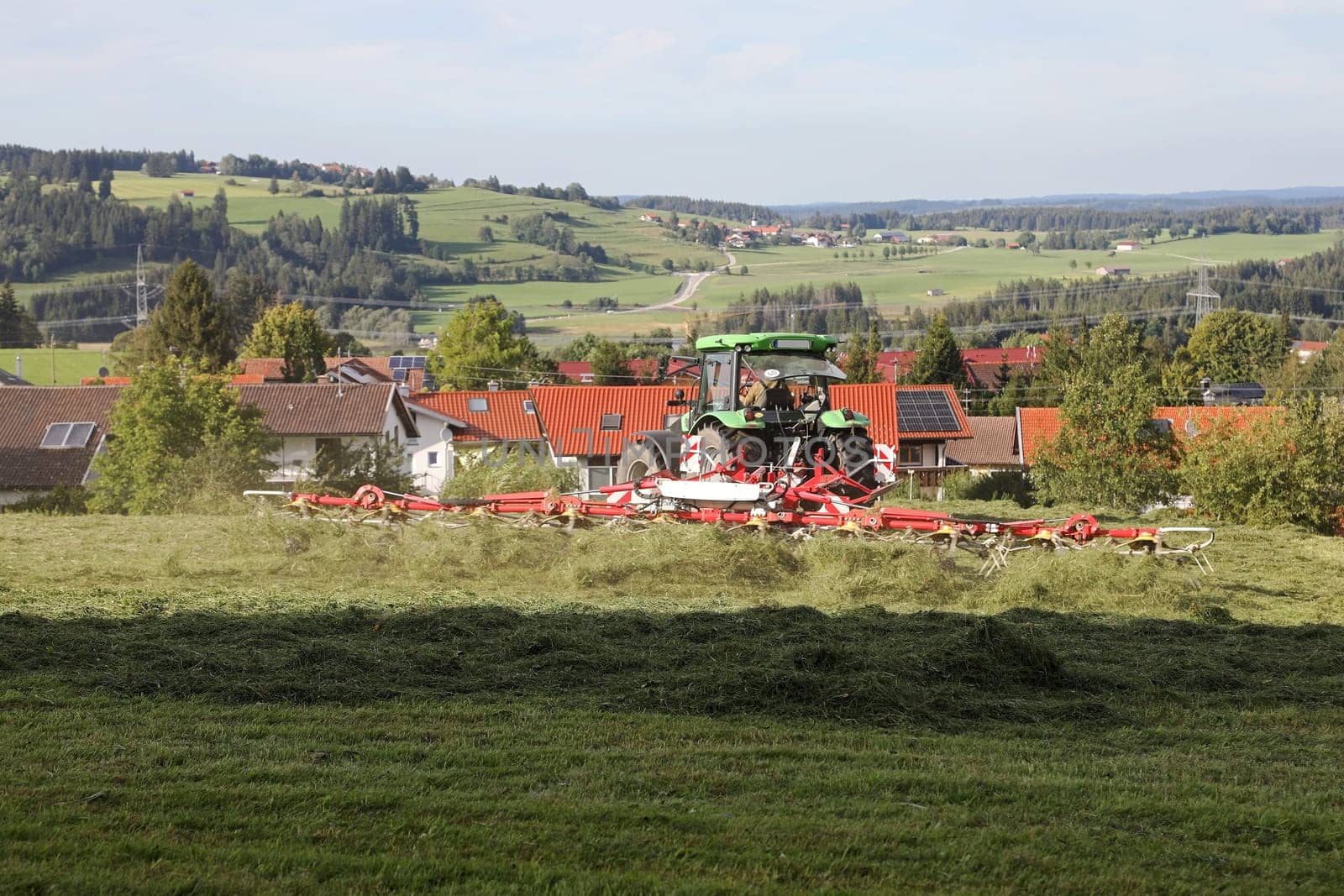 A tractor turns mown hay in a field in a small village