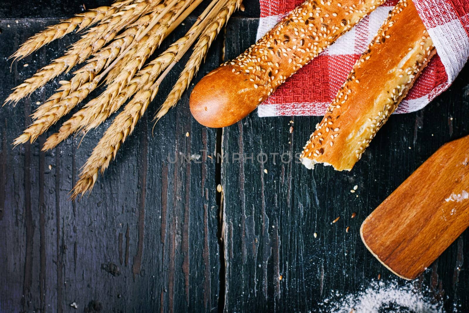 Fresh french baguette bread, organic flour and wholegrain wheat on dark vintage wooden board form above. Top view of traditional baked bread. Bakery shop menu background.