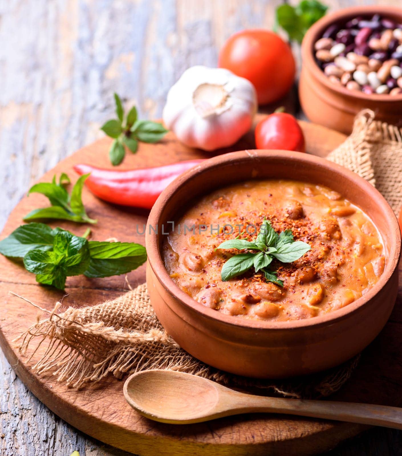Traditional baked beans in tomato sauce cooked in retro clay pot with spices and vegetables. Homemade healthy cuisine.