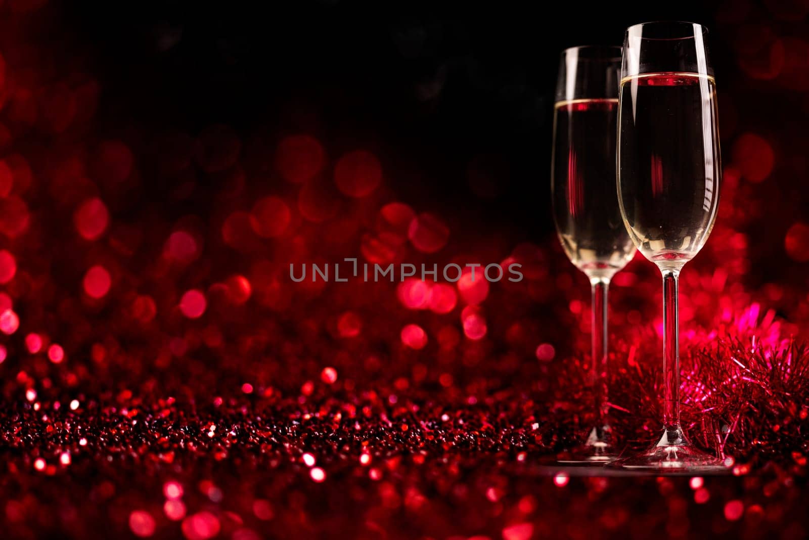 Two champagne glasses on sparkling red bokeh background. Celebration toast flutes. Valentine's day dinner invitation. Christmas and new year holiday party.