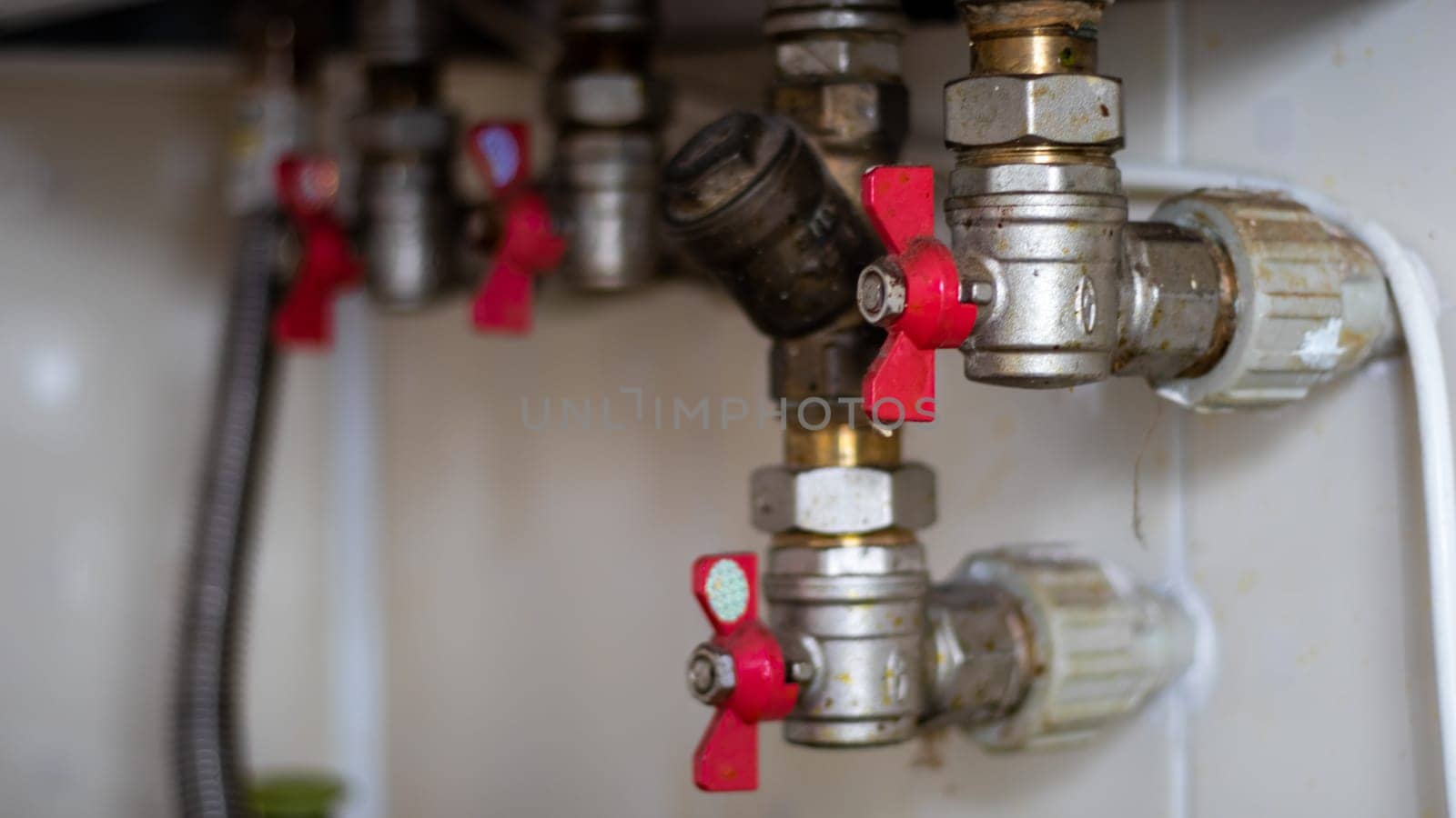 Hidden water taps for connecting a gas boiler on a tiled wall. Plumbing connections for a domestic double-circuit gas boiler. Pipes of the heating system. Installing a gas boiler with red taps