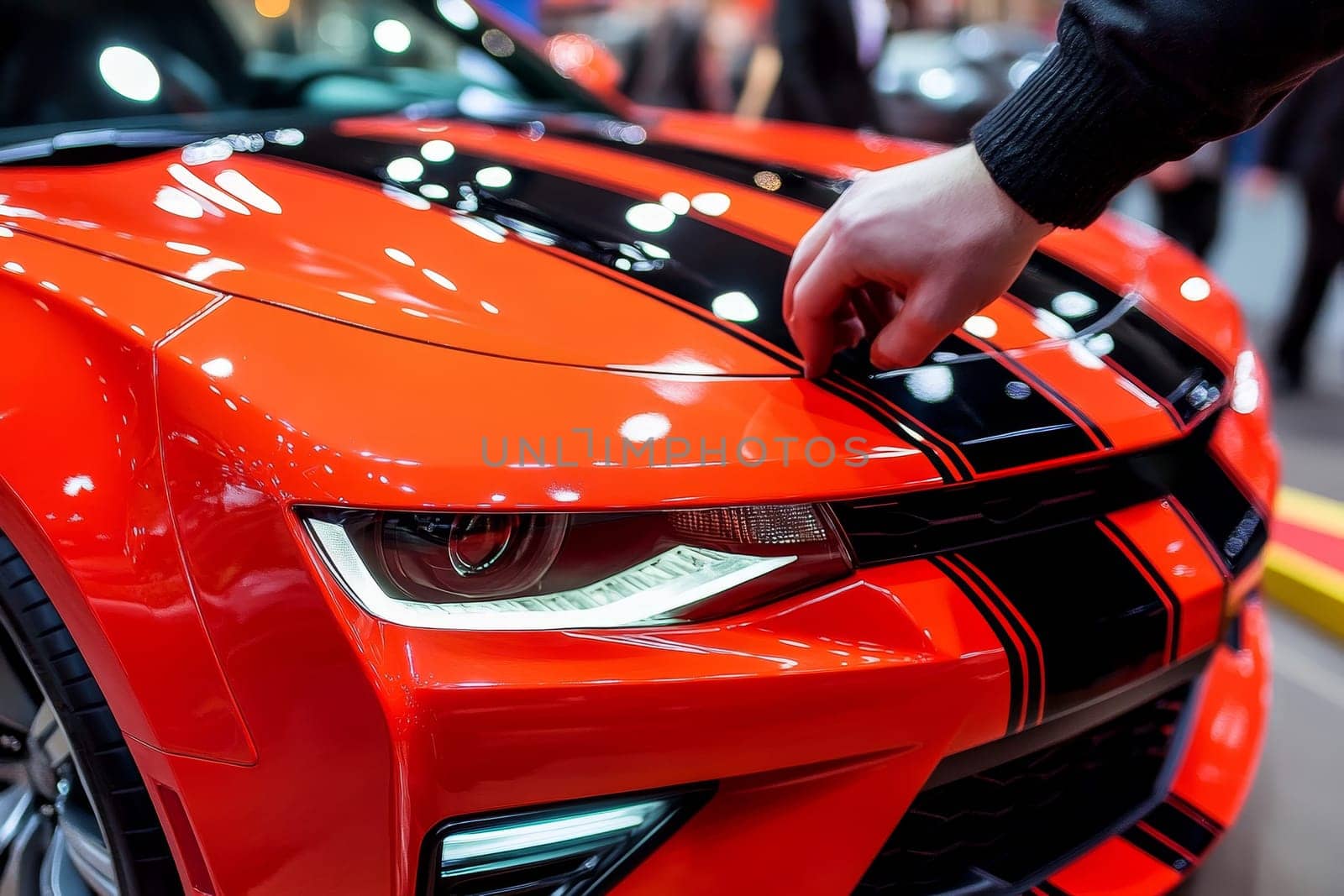 Hand touching the hood of a bright red sports car with black racing stripes at an auto show