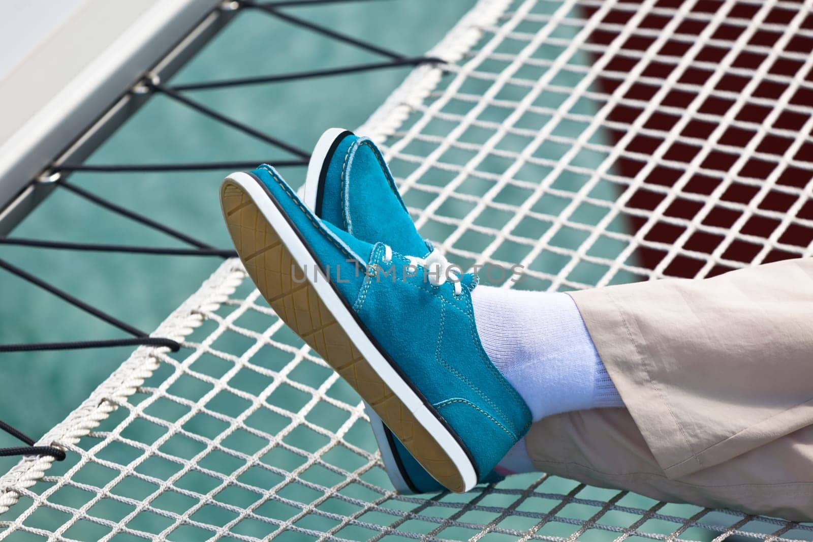 A pair of human legs in pants and bright blue topsiders on yacht hammock background. Yachting