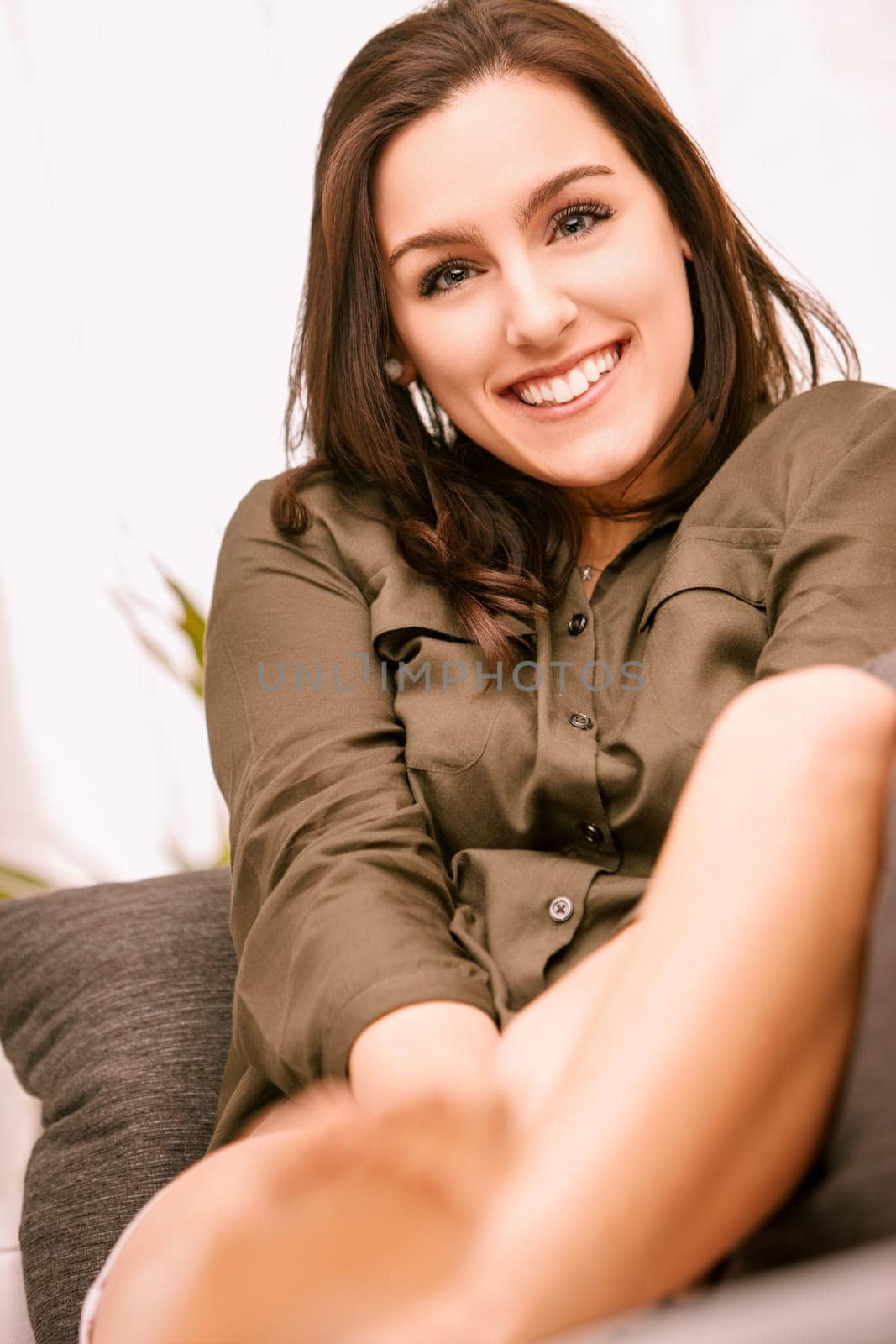 Young woman smiles on her cozy sofa at home, enjoying a relaxing day in casual clothing, embodying a carefree and happy lifestyle