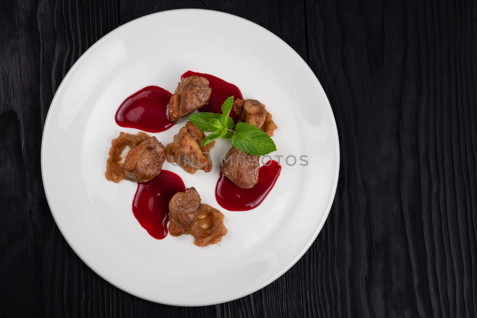 Delicacy Fried pork meat with zucchini puree and berries sauce decorated with mint on white plate on black wooden background