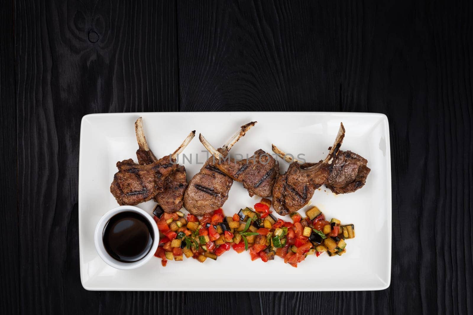Roasted lamb ribs with vegetables on white plate on black wooden background