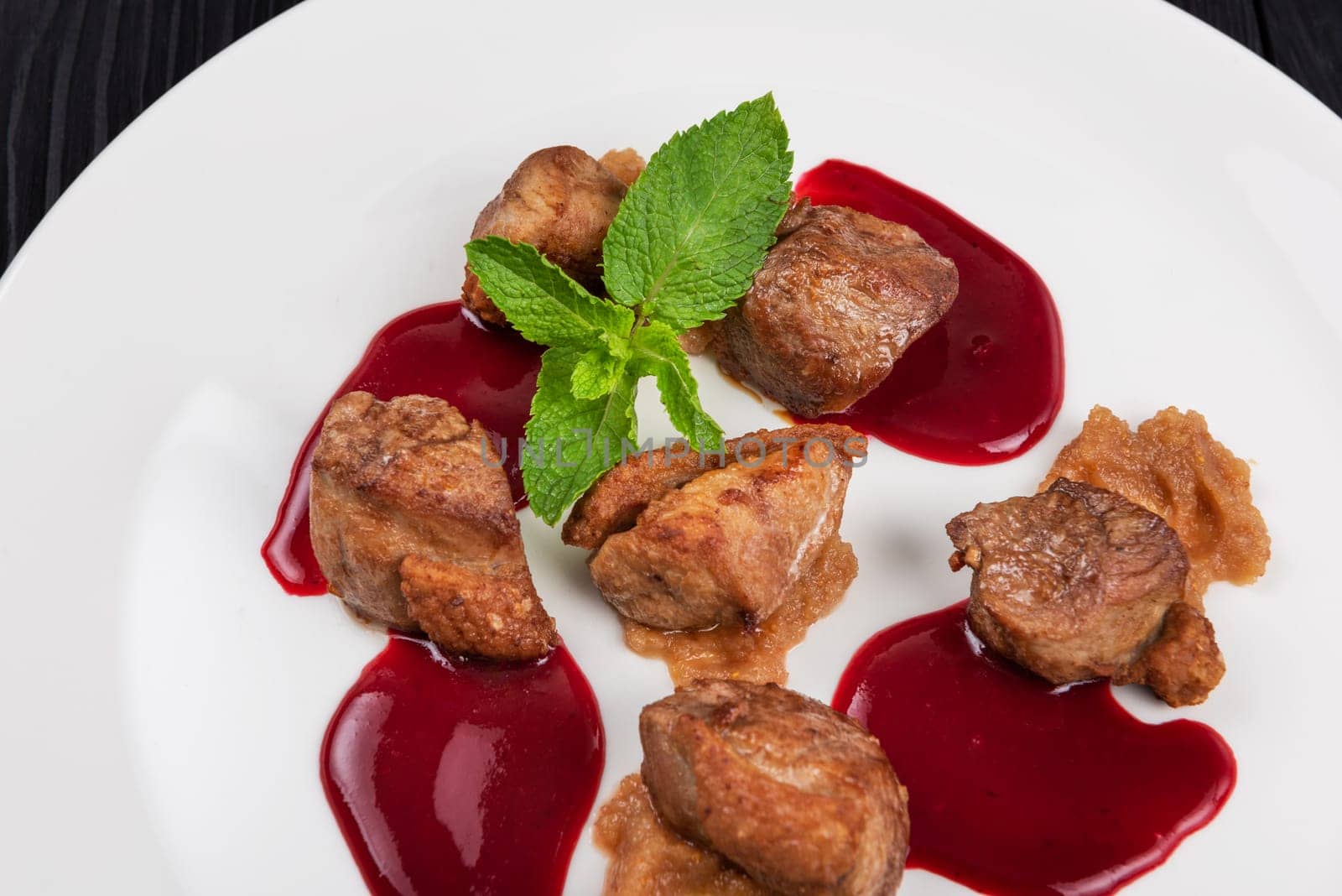 Delicacy Fried pork meat with zucchini puree and berries sauce decorated with mint on white plate on black wooden background