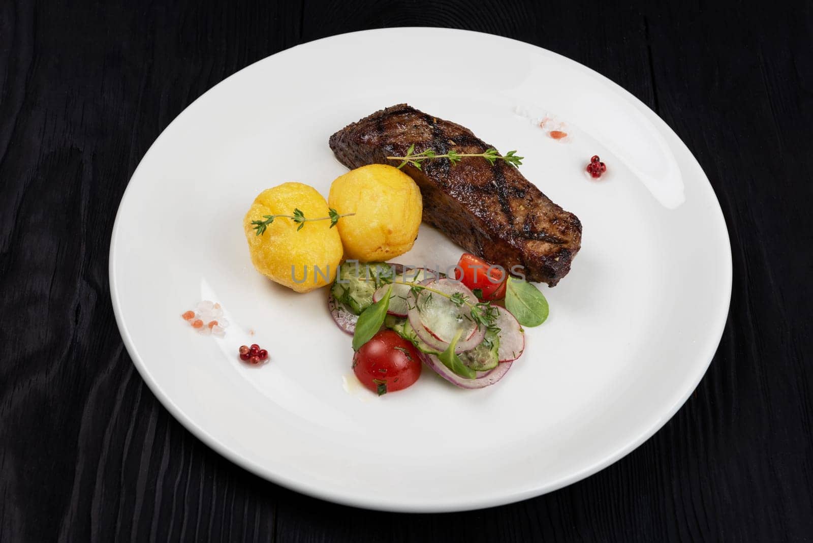 Grilled beef skirt steak meat with potato and vegetables on white plate on wooden black background