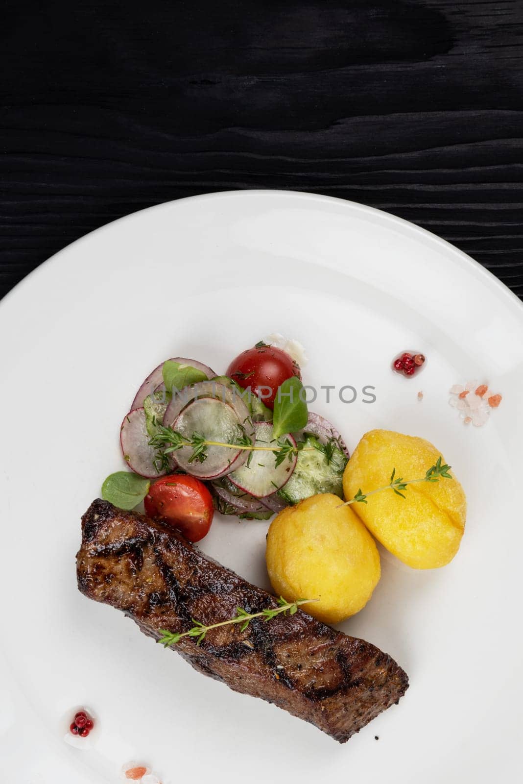 Grilled beef skirt steak meat with potato and vegetables on white plate on wooden black background