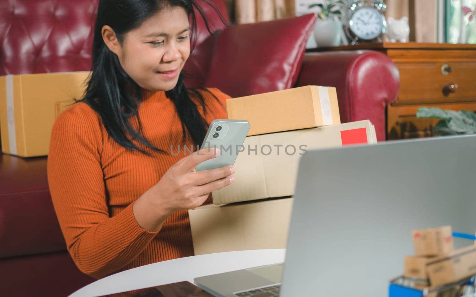 Asia women working business SME online at home her checking order from smartphone  for customer and online delivery for ready packing, Checking orders from customers with digital laptop.