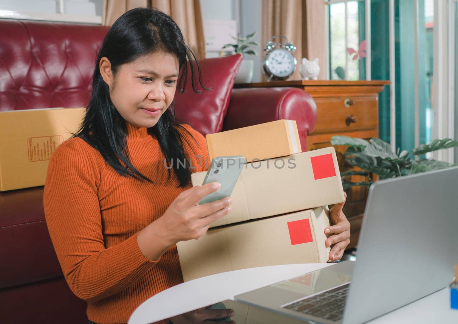Asia women working business SME online at home her checking order from smartphone  for customer and online delivery for ready packing, Checking orders from customers with digital laptop.
