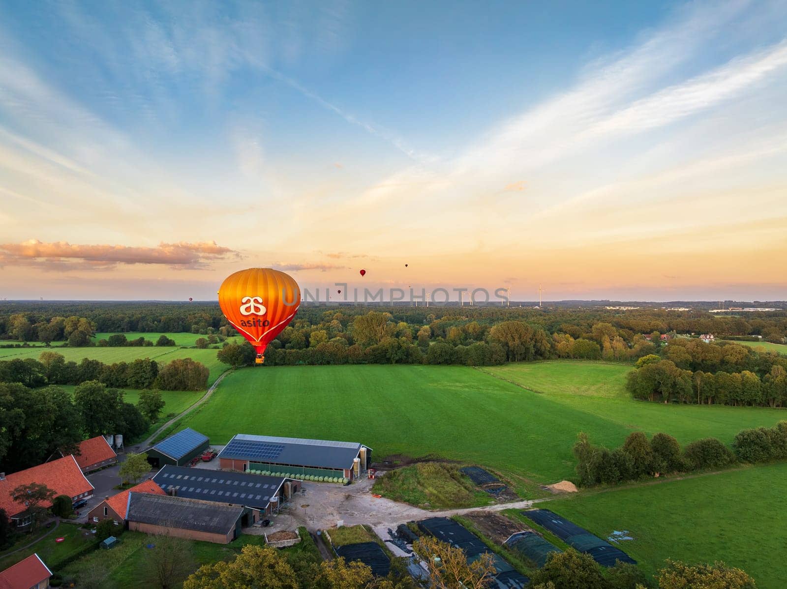 DE LUTTE, NETHERLANDS - AUGUST 21, 2024: Orange hot air balloon searching for a landing spot in a rural landscape