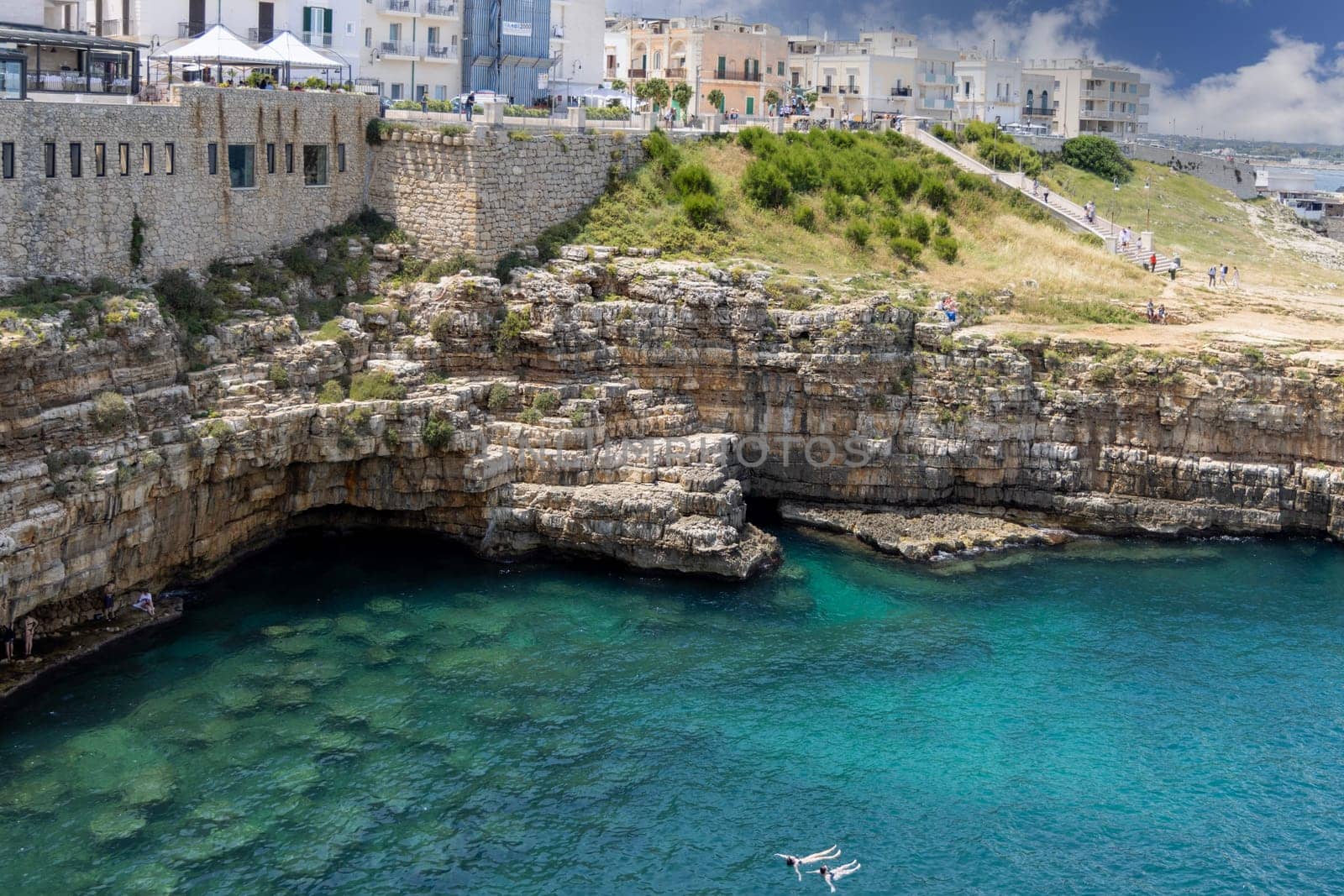 Polignano a Mare, Italy, Apulia - May 24, 2024: Lama Monachile beach, located between picturesque cliffs by Adriatic Sea. People swimming in the water near Grotta Piana