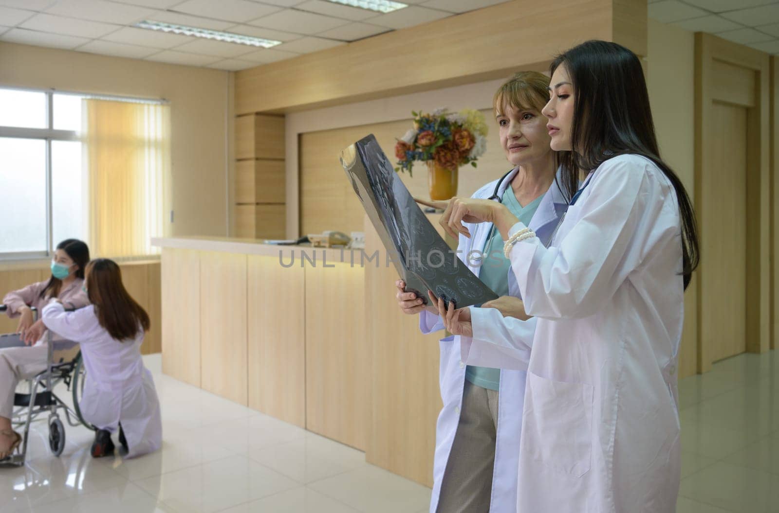 Two women doctor working together examining patient x-ray scan in hospital . Senior doctor and young smiling doctor standing in lobby and discussing diagnosis of brain x-ray results. Healthcare, medicine and insurance concept